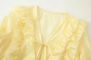 Dettaglio della camicetta in chiffon giallo con maniche a balze e scollo a V con lacci