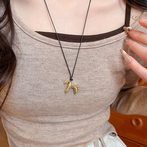 Gros plan d'un collier pendentif chien ballon doré porté sur un pull en maille beige