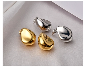 Detailed view of glossy 18K gold and silver teardrop earrings on white silk