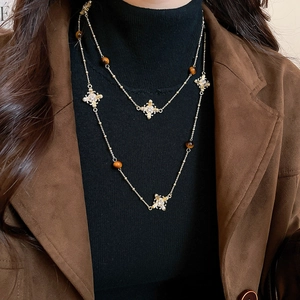 Close-up of double-layered gold necklace featuring tiger eye beads and pavé cross pendants
