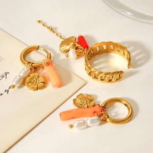 Detail of gold chain ring with coral-pink accent and white pearl dangle charm