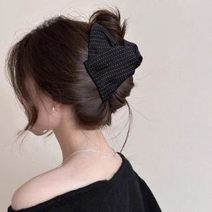 Close-up of black fabric polka dot bow hair claw clip styled on a woman's hair bun