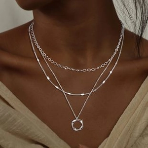 Close-up of a triple layered silver necklace with a twisted circle pendant on a model