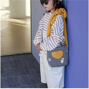 Détail du sac bandoulière à motif pied-de-poule avec patch cœur jaune et breloque ours