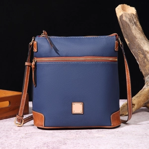 Detail of dark blue pebble leather crossbody bag with brown trim and metal logo plate
