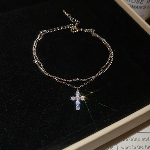 Detail of a double-layer silver bracelet featuring a sparkling zircon cross pendant