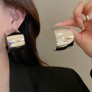 Close-up of minimalist silver wide hoop earrings on model showing high-gloss metallic finish