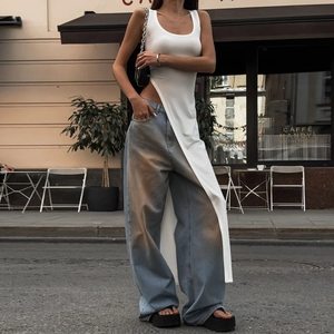 Détail du gilet blanc asymétrique et du jean large bleu délavé porté par le mannequin