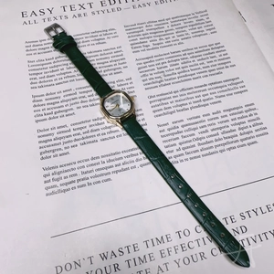 Detail of square gold watch face with green leather strap on vintage paper