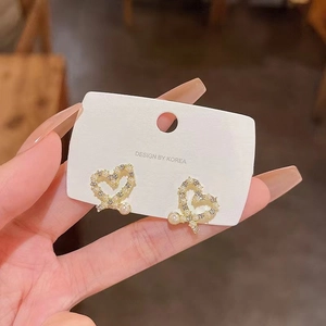 Macro detail of heart-shaped gold earrings with paved crystals and a small white pearl