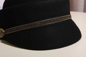 Close-up of black wool newsboy hat with gold braided trim and vintage metal button