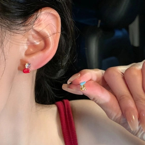 Close-up view of exquisite asymmetric colorful zircon stud earrings shown on ear and hand