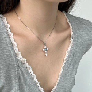 Detail of cross pendant necklace featuring opal stones and blue gem on box chain