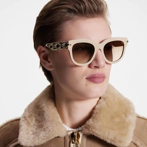 Close-up of beige oval sunglasses featuring gold metal temples with cross texture