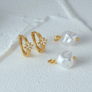 Detail of star-shaped golden earrings with micro-set diamonds and baroque pearls