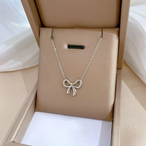 Silver bow pendant necklace elegantly presented in a gold-toned jewelry box with fabric