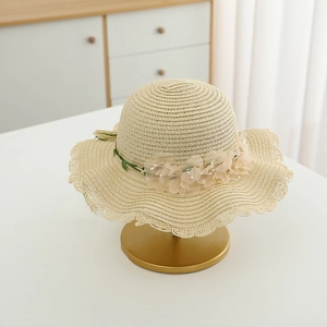 Detail of beige straw hat featuring delicate pink fabric flowers and wavy brim design