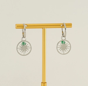 Detail view of silver hollow sun pendant earrings with a small green stone on a stand