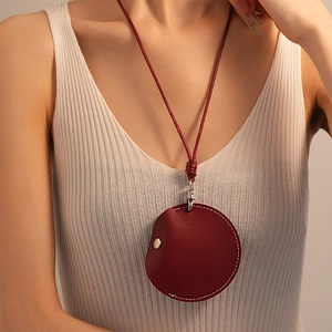 Close-up of a retro reddish-brown round leather pouch necklace with white stitching detail