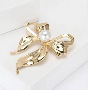 Elegant gold bow brooch with a central white pearl on a clean minimalist background