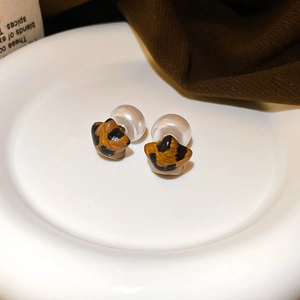 Detailed view of leopard print earrings with white pearl backings on a ceramic plate