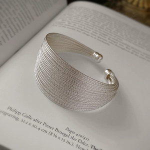 Detail of multi-layer silver metal cuff bracelet featuring textured woven strands on open book