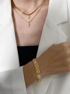Close-up of layered gold snake chain necklaces with crystal R pendant and wide bracelet