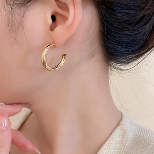 Gros plan d'une boucle d'oreille en métal doré en forme de C sur un modèle au ton chaud doux