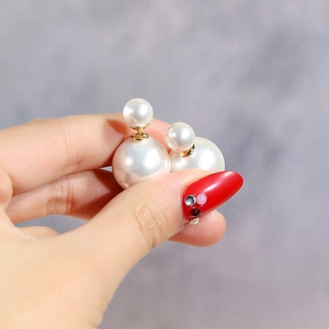 Detail of double pearl stud earring with white faux pearls and gold finish on fingers