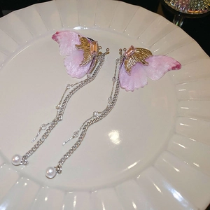 Détail de boucles d'oreilles papillon en tulle rose avec pompons argentés et perles