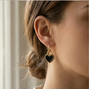 Close-up of golden hoop earring with a black heart pendant on female model