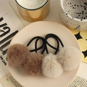 Set of four fluffy faux fur pom pom hair ties in brown and beige on a ceramic tray