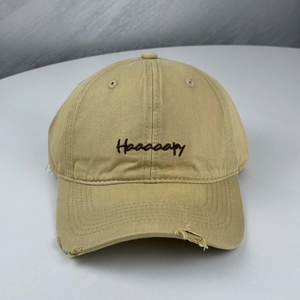 Close-up of khaki baseball cap with distressed brim and Haaaaapy letter embroidery