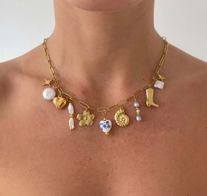 Detail of gold chain necklace with pearl, heart, and star charms worn by a model