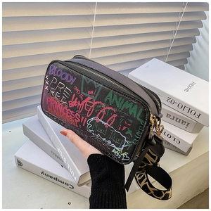 Detail of crossbody camera bag featuring vibrant street graffiti and wide woven strap