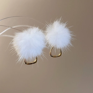 Macro detail of white plush pom-pom earrings with elegant gold metal buckles