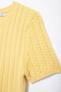 Dettaglio del maglione giallo a trecce che mostra il girocollo e l'etichetta