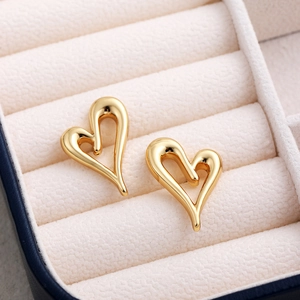 Detailed shot of hollow 18K gold heart studs on a white jewelry cushion display
