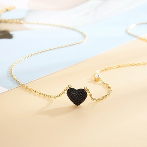 Détail macro du collier doré avec pendentif cœur noir serti et petite pierre zircone