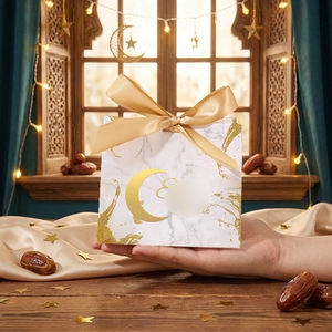 Handheld view of marble textured Ramadan gift box with gold crescent and ribbon detail