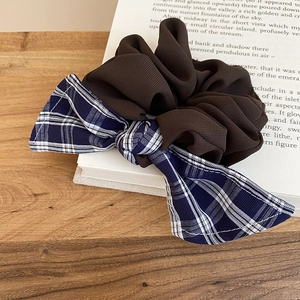 Detail of a brown fabric scrunchie with a blue and white checkered bow on a wooden table