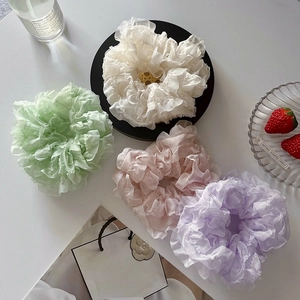 Macro detail of four pastel pleated organza hair scrunchies with elegant gold metal charms