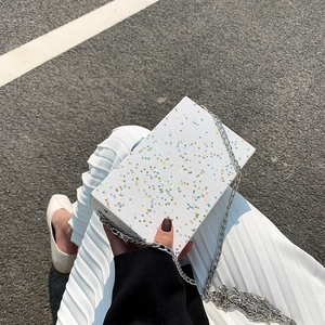 Glossy white box bag with colorful stars and silver chain strap shown in outdoor setting