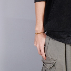 Close-up of a gold stainless steel Cuban link bracelet worn on a male model's wrist