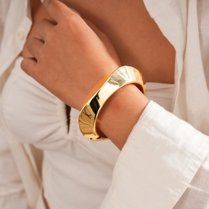 Detail of chunky gold irregular wave bangle featuring high-polish finish on female wrist