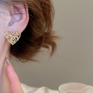 Detailed close-up of golden heart-shaped stud earrings with hollow design and zircons