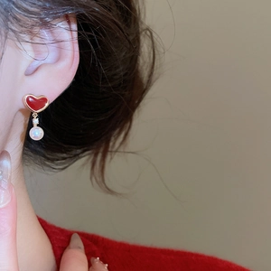 Close-up of red enamel heart earrings with pearl drops and gold trim on model