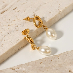 French vintage baroque pearl earrings with golden knot design on a beige stone surface