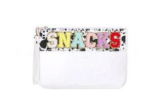 Detail of SNACKS chenille patches on a clear PVC toiletry bag with gold zipper and cow print