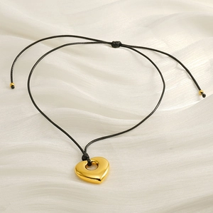 Detailed close-up of a heart-shaped gold pendant on a black cord over white silk fabric